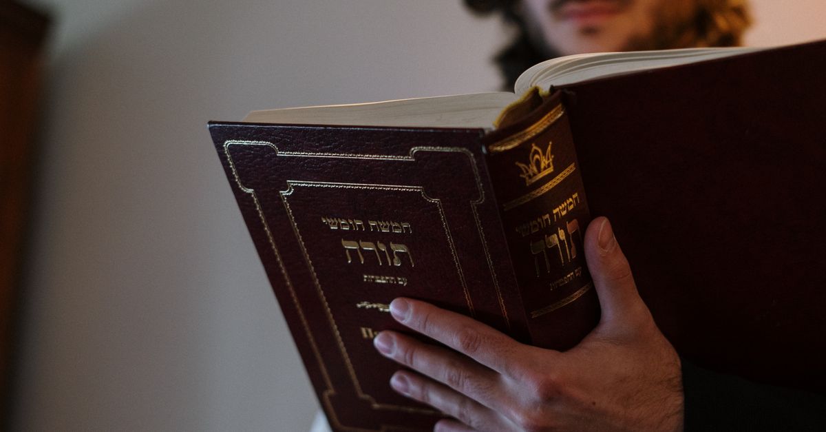 Orthodox Jewish man reading Torah with Hebrew text during Shabbat indoors, emphasizing tradition and culture.